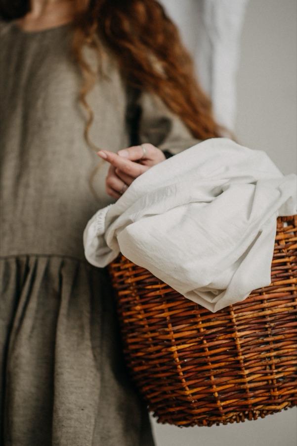 Mulher com vestido de linho a transportar um cesto de verga com roupa de linho
